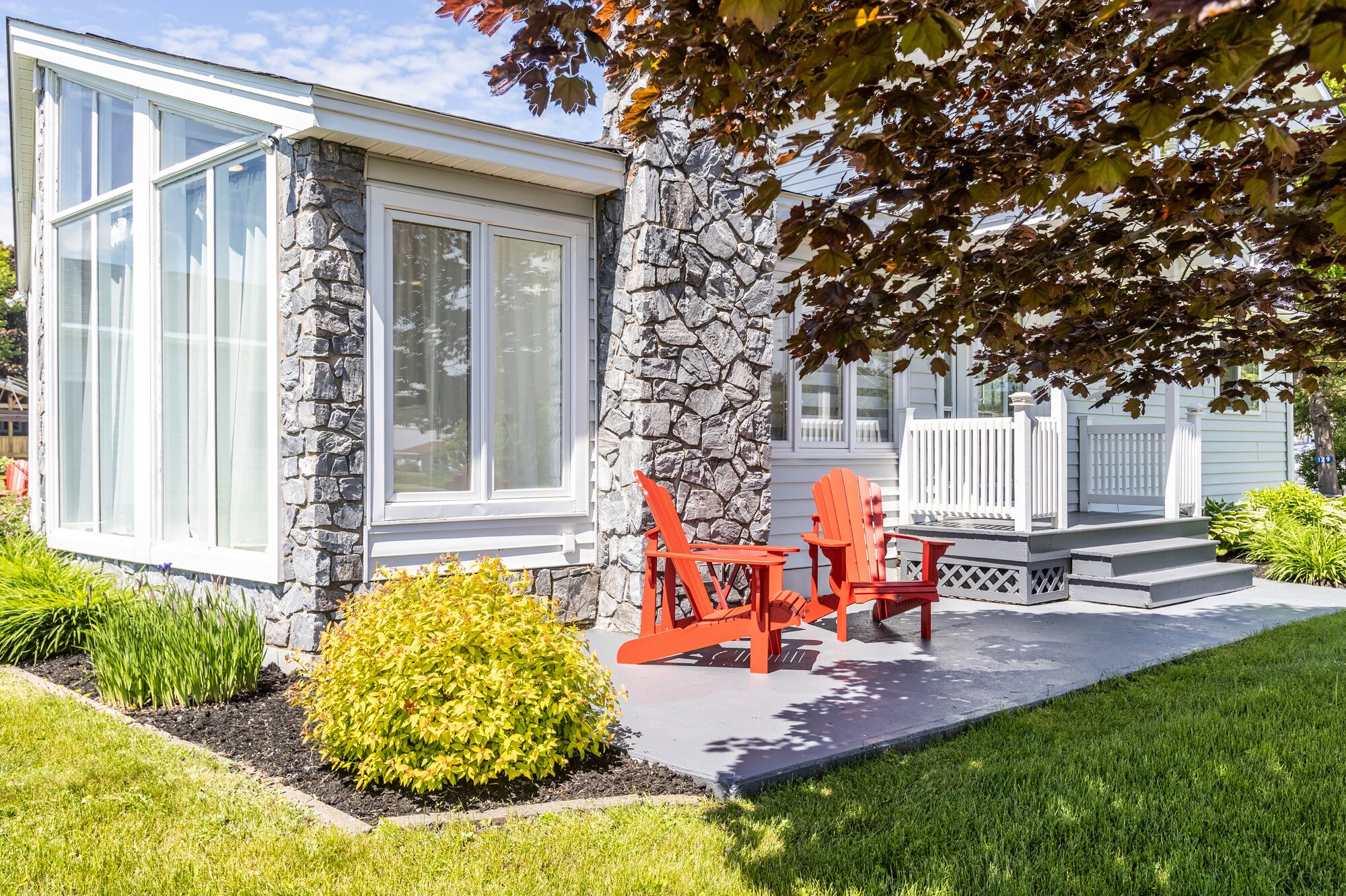 Red Adirondack chairs on a stone-and-concrete patio beside the sun-filled dining room.