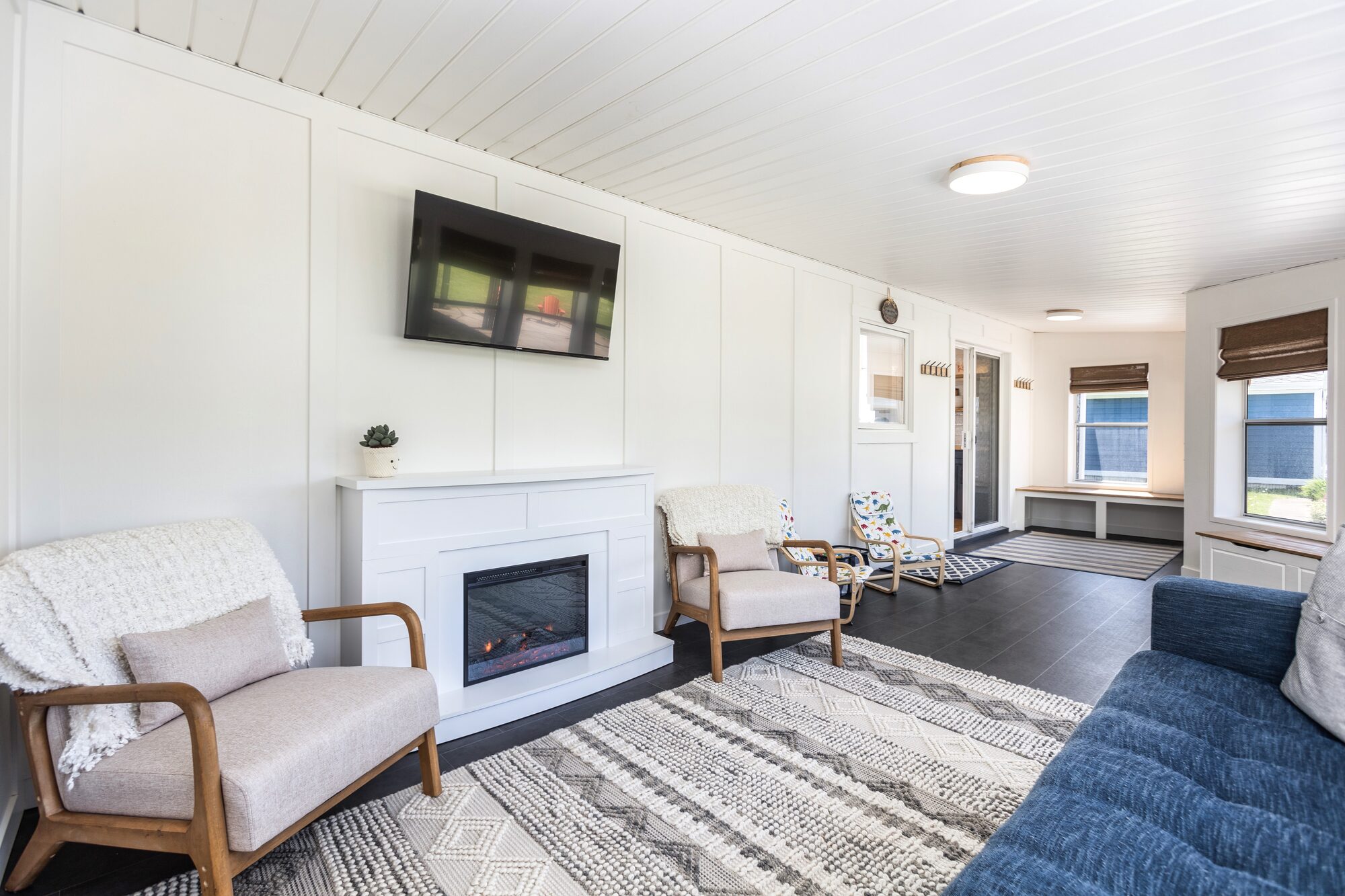 The downstairs sunroom with a fireplace, TV, two cozy armchairs, storage benches, and the navy queen sofa bed at right.